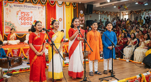 Bangladeshi children dressed up in traditional colorful boishakhi outfits singing Bengali rhymes together with microphones on decorated stage, festive atmosphere